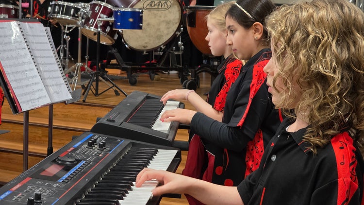 Students wearing red band shirts and playing keyboards