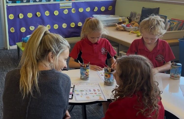 three childrne sitting with a teacher around a table engaged in reading.