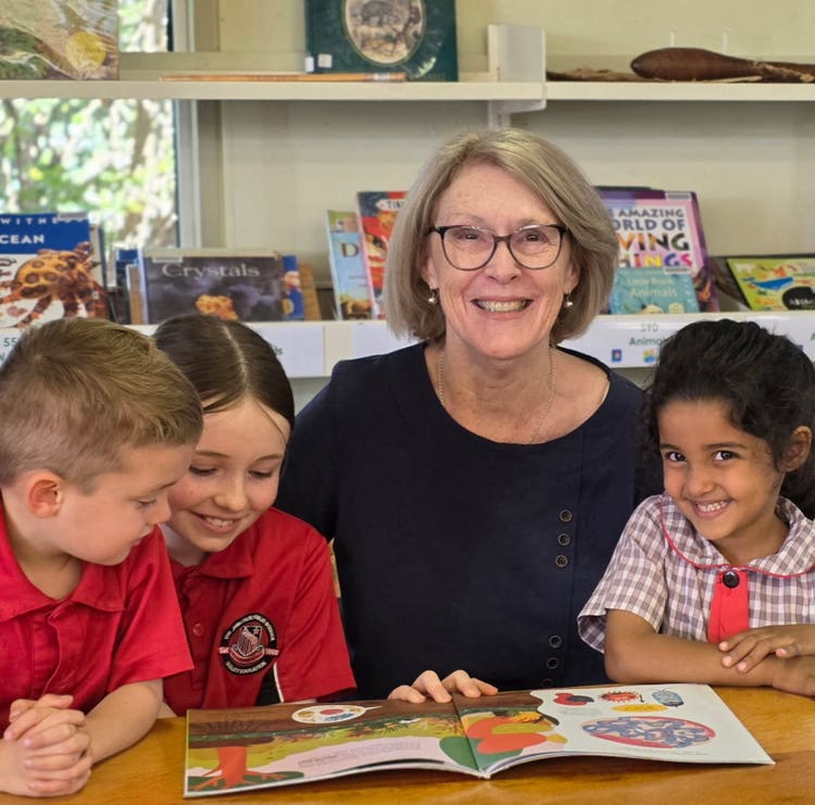 Prinicpal sitting at desk with three students. Students are reading a book together.
