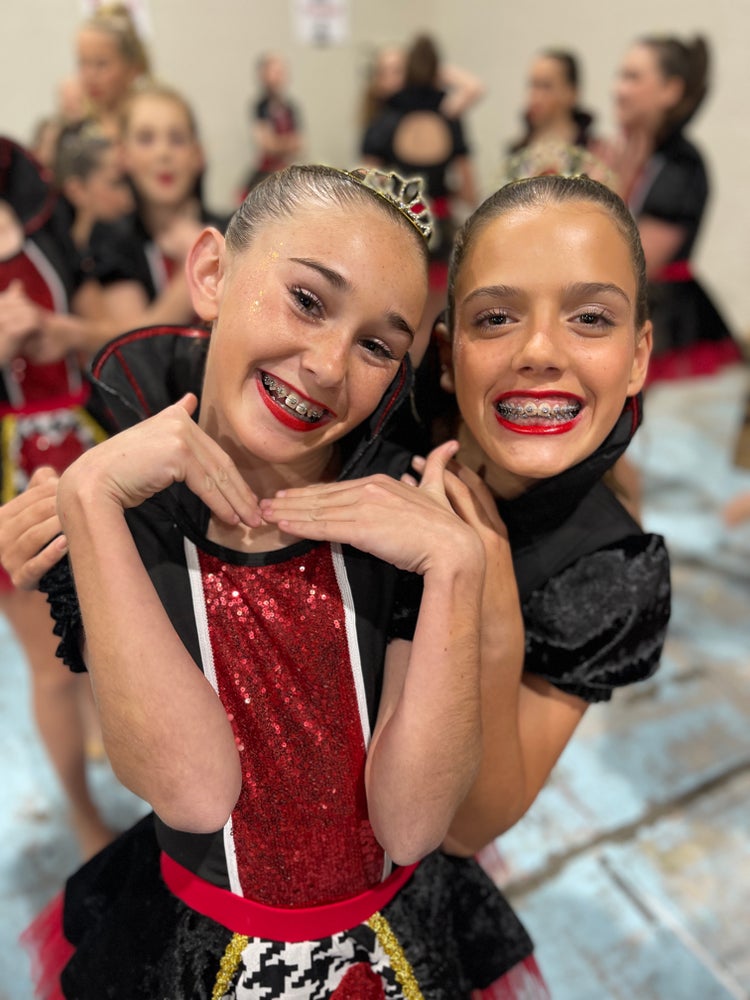 Two girls dressed in dance costumes wearing tiaras on their heads.